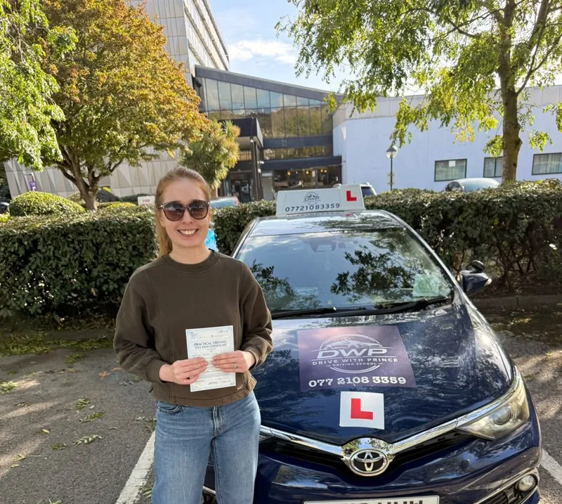 A DWP Driving School pupil with a test pass certificate in front of DWP Driving School's navy learner car and its roof sign