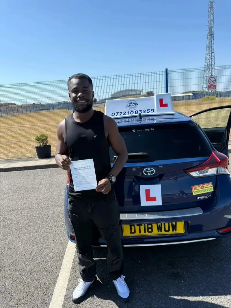 A DWP Driving School pupil with a test pass certificate behind DWP Driving School's navy learner car, its roof sign showing the school's phone number