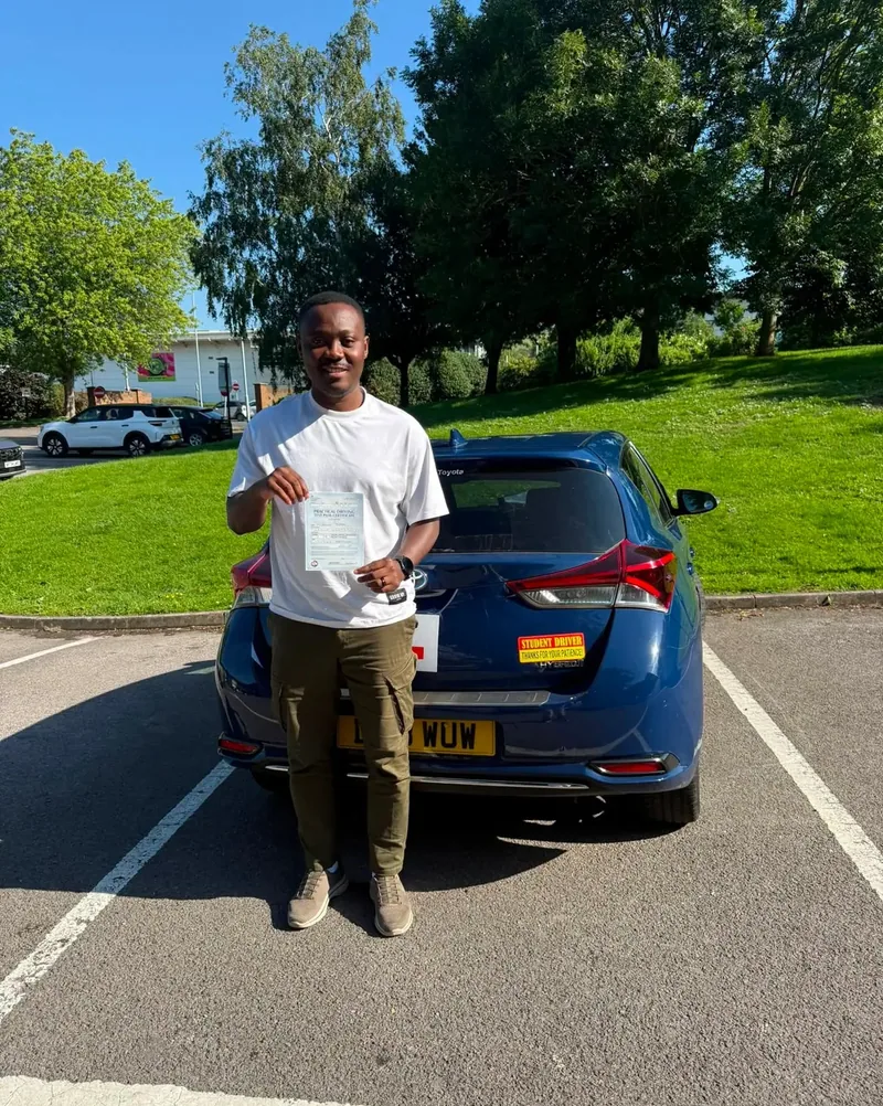 A DWP Driving School pupil holding a test pass certificate behind DWP Driving School's navy learner car