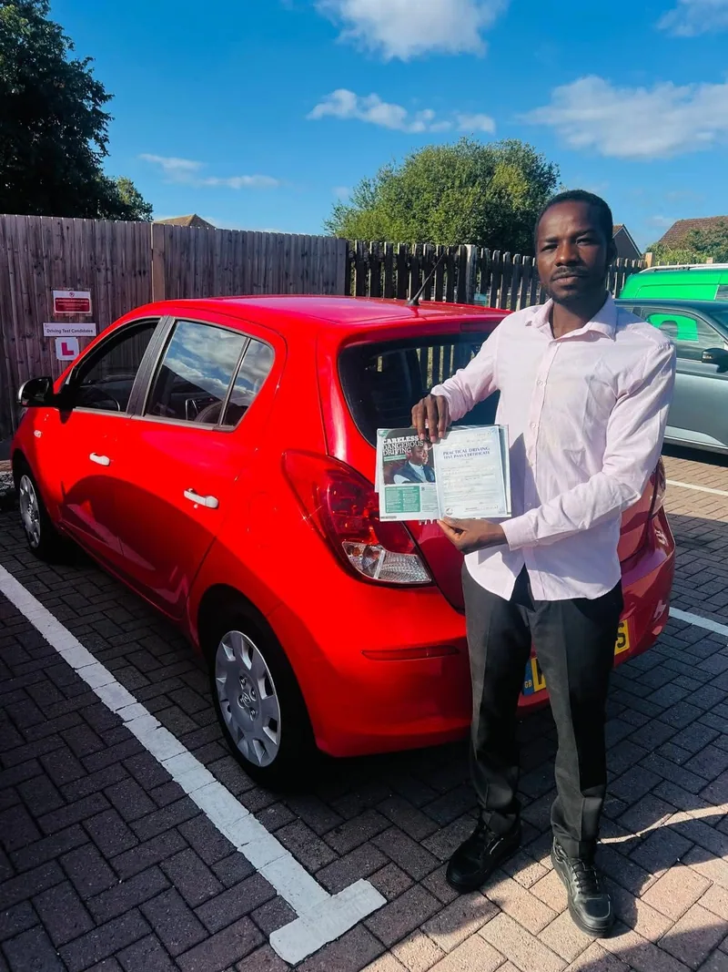 A DWP Driving School pupil holding a test pass certificate beside a red car